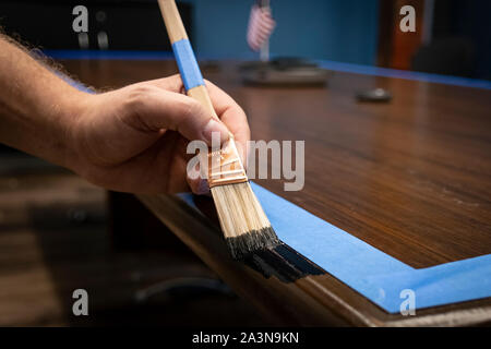 Hand painting conference table edge/trim; prepped with blue painter's tape Stock Photo