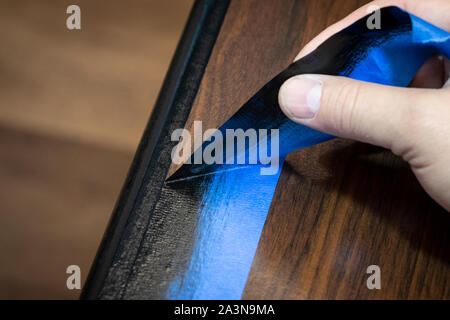 Hand removing blue painter's tape from edge of refinished furniture paint job. Stock Photo