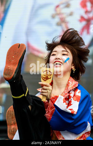 Hinokuni Yosakoi festival in Japan. Close up of smiling young woman dancer holding naruko, clapper, and kicking her leg up high, wears Jika-tabi shoe. Stock Photo