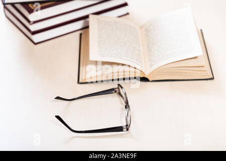 reading book with low vision - spectacles and open book near stack of books on pale table (focus in the foreground) Stock Photo