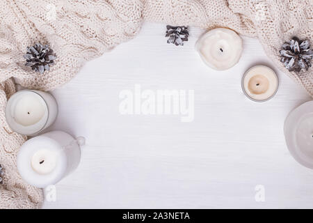 Knitted sweater or scarf, candles and pine cones on white bakground. Creative frame with place for text Stock Photo