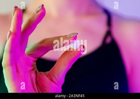 Woman's hand close-up holding drug pill in neon light of nightclub Stock Photo