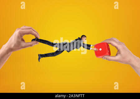 Big male hand holding tiny businessman who is reaching to another big hand holding red casino dice on yellow background Stock Photo