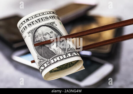 Chinese sticks hold one dollar on the background of smartphones. Concept on the theme of the economic confrontation between America and China. Trade w Stock Photo