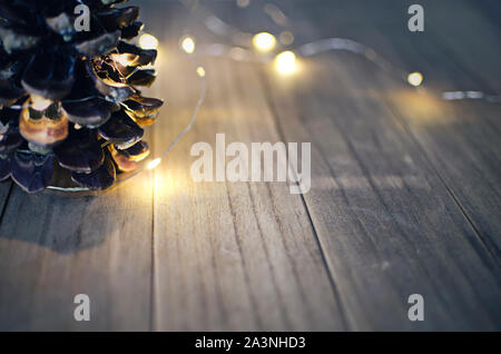 Detail of a pinecone on a wooden table with bokeh lights in a blurred background. Selective focus on a light in the pinecone. Stock Photo