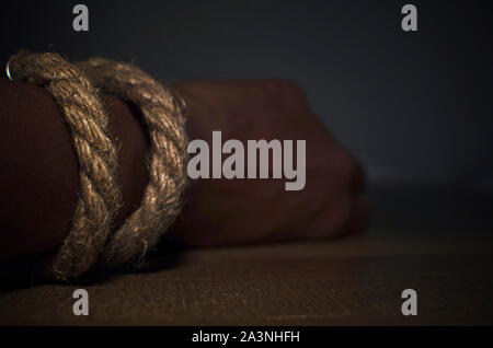 Hand bound by rope of a black woman lying on a wooden table. Selective focus on rope. Blurred background. Stock Photo