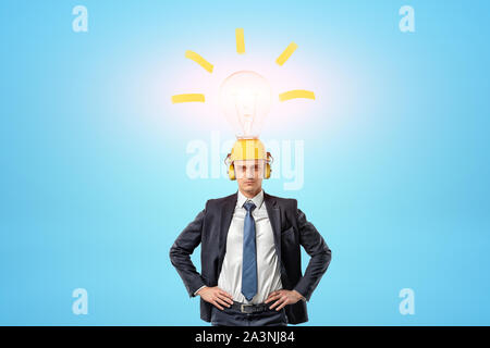 Businessman wearing yellow safety helmet with light bulb above on blue background Stock Photo