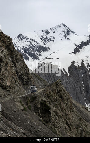 Beautiful view of a lone vehicle on a steep climb on Zoji La Pass against massive snowcapped mountains, Srinagar - Leh Highway, Jammu and Kashmir Stock Photo