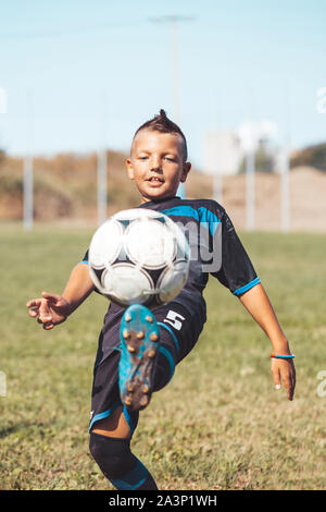 Little boy with soccer ball doing flying kick at stadium. Kid soccer player in motion on green grass background. Junior football player in action, jum Stock Photo