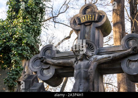 Beautiful stone Jesus Christ crucifixion statue on grave from 19th century during sunset with common ivy in background, shallow depth of field, Olsany Stock Photo