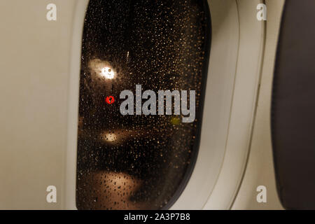 raining water drop on glass of window frame of aeroplane window inner airplane and blur background with red, gold and yellow circle round light bokeh Stock Photo