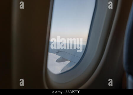 Close up interior view windows inside airplane cabin and background of dawn or dusk sky and aerial view of airplane's wing and engine over sky. Stock Photo