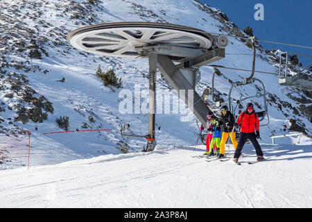 PYRENEES, ANDORRA - FEBRUARY 13, 2019: A group of skiers in colorful clothes walk off the chairlift at the top. Snow covered slope and metal structure Stock Photo