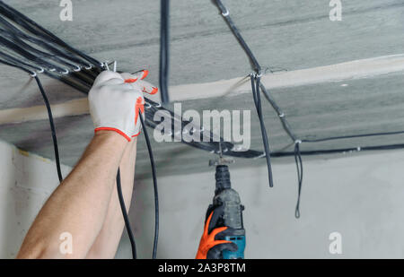 Electrician's hands are fixing electrical cables to the ceiling. Next is that the electrician's hands drill the ceiling. Stock Photo