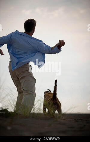 Mature adult man throwing a stick for his dog on a beach. Stock Photo