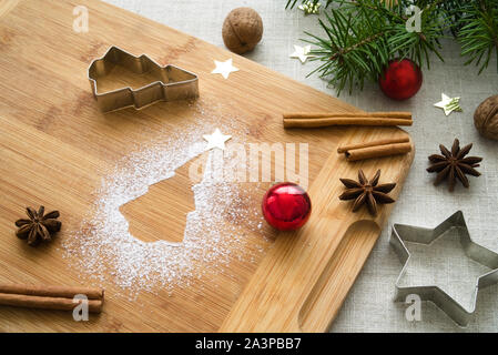 Christmas composition around a shape of Christmas tree of powdered sugar, wooden board with traditional festive attributes. Christmas mood background Stock Photo