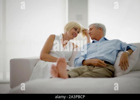 Happy couple looking at each other lovingly while sitting on a couch in their living room. Stock Photo