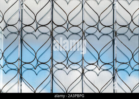 Decorative openwork metal mesh on the window for protection. The window glass reflects the grid pattern Stock Photo