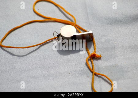 Chromed children's whistle with a tied yellow rope exposed on the table Stock Photo
