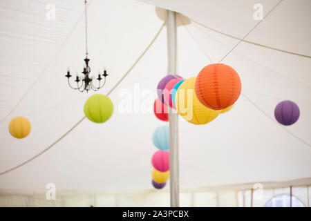 Colourful paper lanterns hung along the ceiling of the wedding reception tent Stock Photo