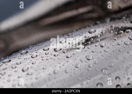 Close up and macro view of raining water drops on shiny polished curvature chrome surface of abstract sculpture. Stock Photo