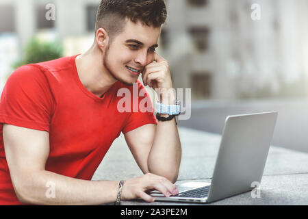 Young attractive guy who is smiling looking at his laptop screen . Young man using laptop. Stock Photo