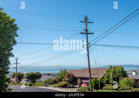 PG&E power lines and cables intersect at a power pole in an El Cerrito, California, neighborhood. San Francsico Bay and downtown are in the distance. Stock Photo