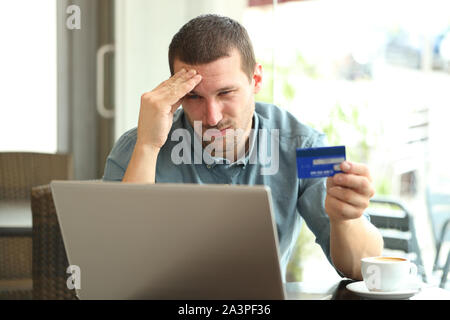 Frustrated man paying with credit card and laptop sitting in a coffee shop Stock Photo
