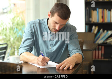Concentrated man writing notes in a paper sheet using a pen sitting in a coffee shop Stock Photo