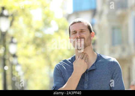 Stressed man suffering throat ache standing alone in the street Stock Photo
