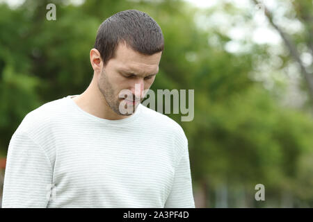 Sad man walking alone looking down complaining in a park Stock Photo
