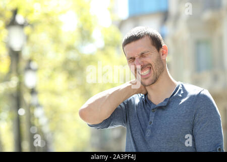 Stressed adult man suffering neck ache standing alone in the street Stock Photo