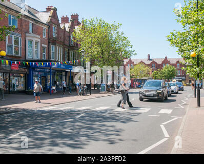 Cars waiting whilst two young ladies walk across the road on a Zebra Crossing on a sunny day in Lytham Lancashire England UK Stock Photo