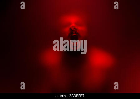 Red color filter version of Creepy man screaming behind the frosted glass. Stock Photo