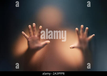 Creepy man looking behind the frosted glass and holding it with two hands. Stock Photo