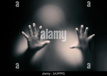 Black color version of Creepy man looking behind the frosted glass and holding it with two hands. Stock Photo