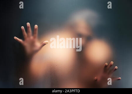 Creepy man looking behind the frosted glass and holding it with two hands. Stock Photo