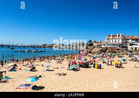 View of the crowded pretty little beach named Praia da Conceicão along the beach promenade between the towns of Estoril and Cascais, nearby Lisbon, Po Stock Photo