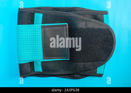 Close up of black medical waist belt for back pain isolated on blue background. Top view. Stock Photo