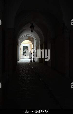 A young Tunisian couple walking through a covered pedestrian alleyway in streets of the Hafsia quarter of the Medina (old city) of Tunis, Tunisia. Stock Photo