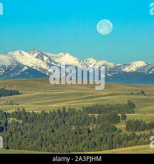 full moon setting over the flint creek range and foothills of upper spotted dog creek basin near avon, montana Stock Photo