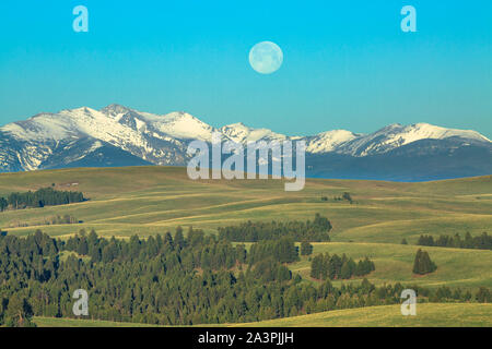 full moon setting over the flint creek range and foothills of upper spotted dog creek basin near avon, montana Stock Photo