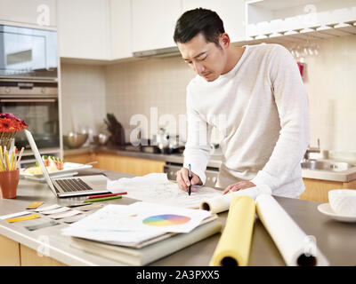 young asian designer working at home drawing on drafting paper on kitchen counter Stock Photo