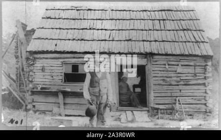 Stephen Steptoe, Junior, three-quarter length portrait, standing, facing front, in front of cabin with woman in doorway Stock Photo