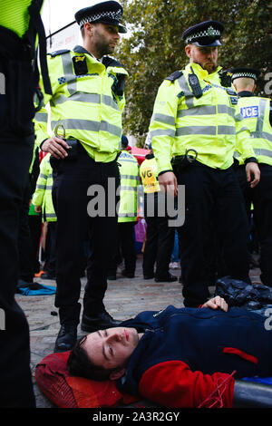 Police officers surround a member of climate change activist movement, Extinction Rebellion (XR) protesting on Victoria Street during the third day of the group's 'International Rebellion' in London.Police officers continue to clear demonstrators and tents from sites across Westminster, with activists having been warned about moving to a designated protest area around Nelson's Column in Trafalgar Square or face arrest. Similar blockades by Extinction Rebellion in April, at sites including Oxford Circus and Waterloo Bridge, saw more than 1,000 arrested, a tactic promoted by XR founder Roger Hal Stock Photo