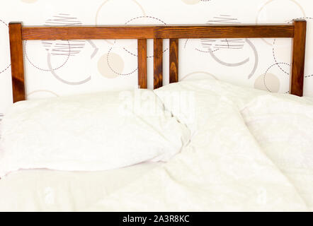 the unmade bed with white rumpled pillows at the head of the wooden bed Stock Photo
