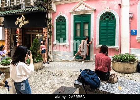 Macau, China - October 15 2018: Asian female tourist posinging for photo in front of the famous colorful facade in the traversa da paixao, or love lan Stock Photo