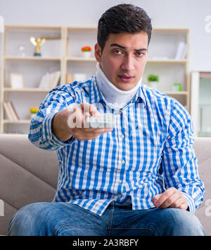 Man with a head neck spine trauma wearing a neck brace cervical collar watching tv at home Stock Photo