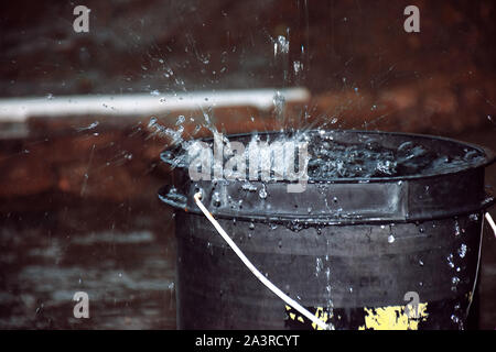 Rainy weather on the terrace in summer. The rain falls into the bucket and creates splashes Stock Photo