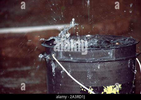 Rainy weather on the terrace in summer. The rain falls into the bucket and creates splashes Stock Photo